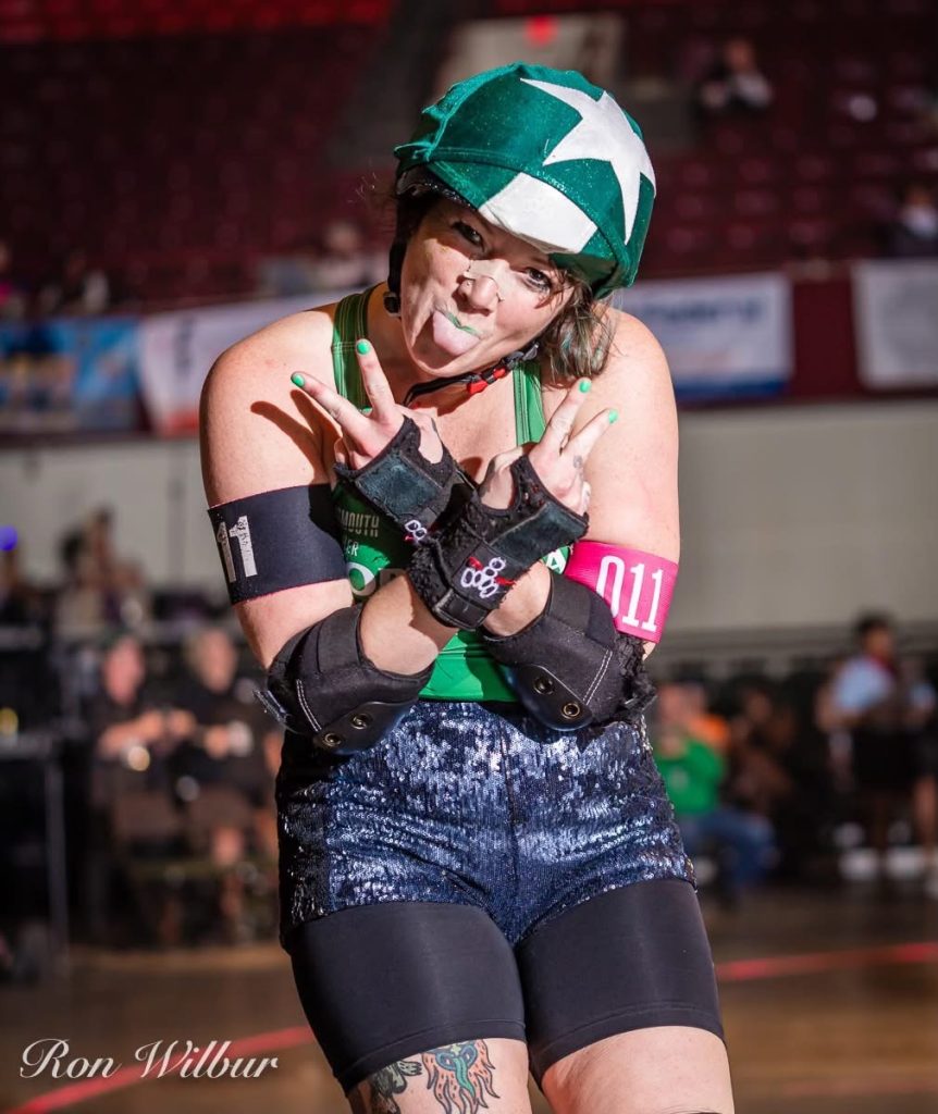 Baller has her arms crossed with double peace signs and her tongue is stuck out